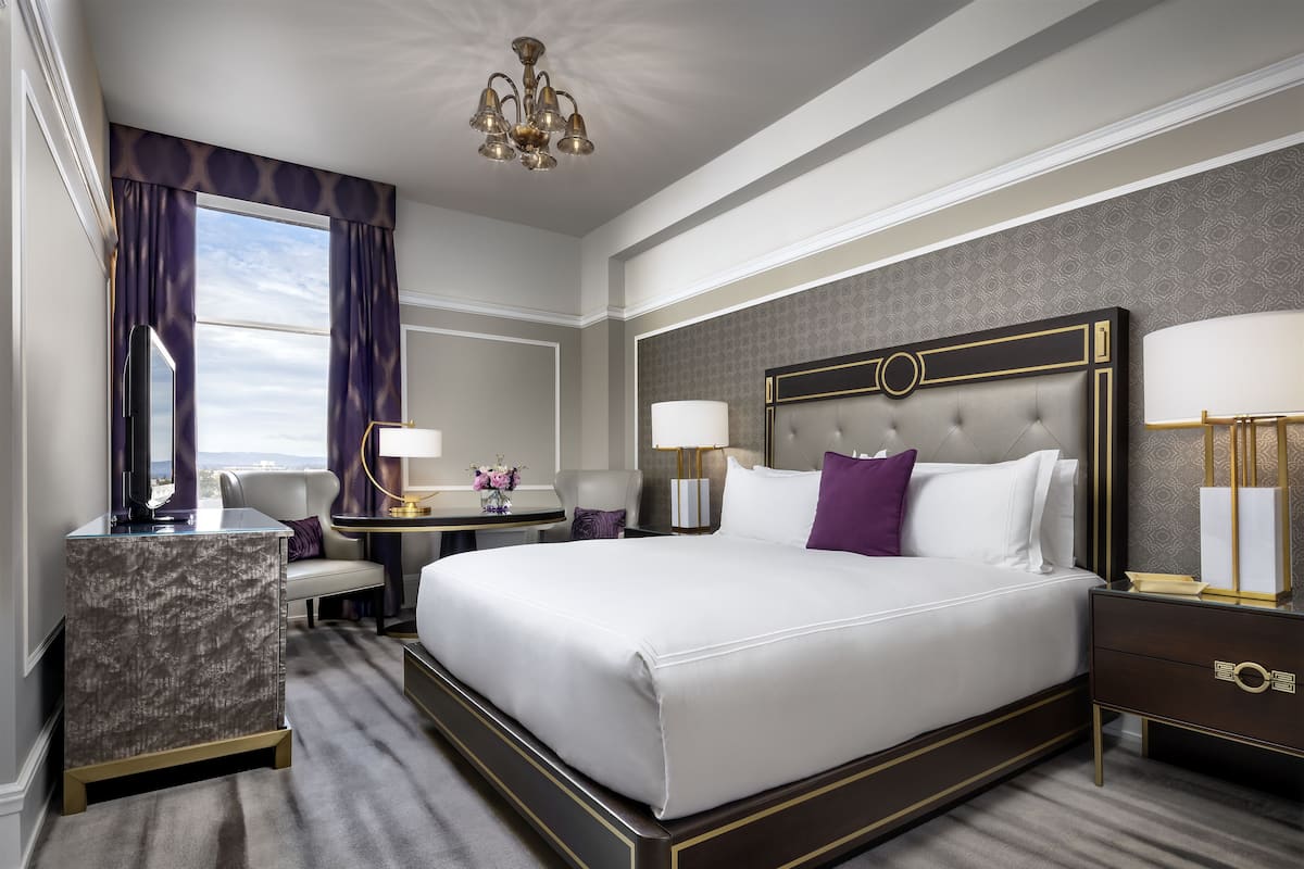 A spacious hotel room with a large bed, a desk, a chair, and a television.