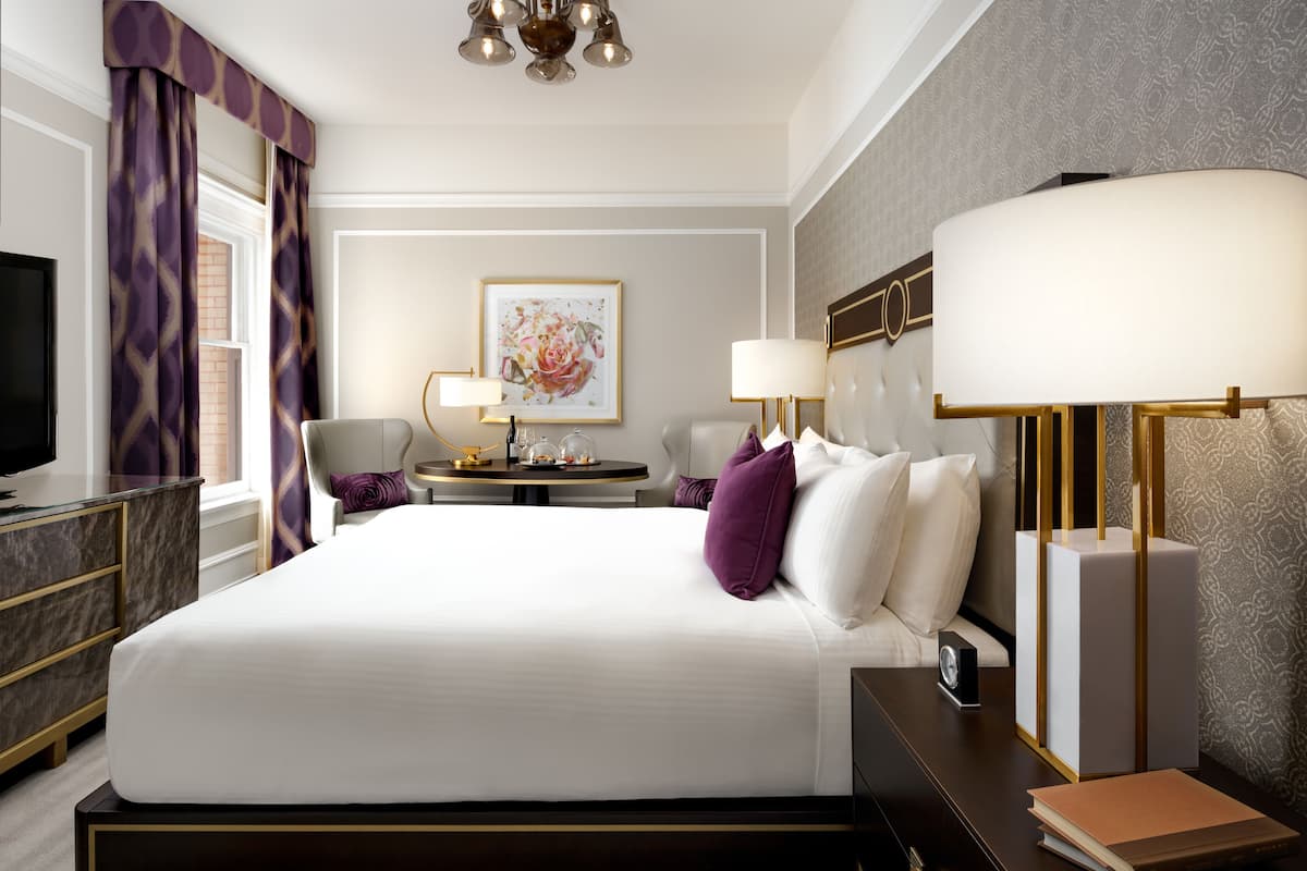 A hotel room with a large bed, a desk, a chair, a television, and a lamp.