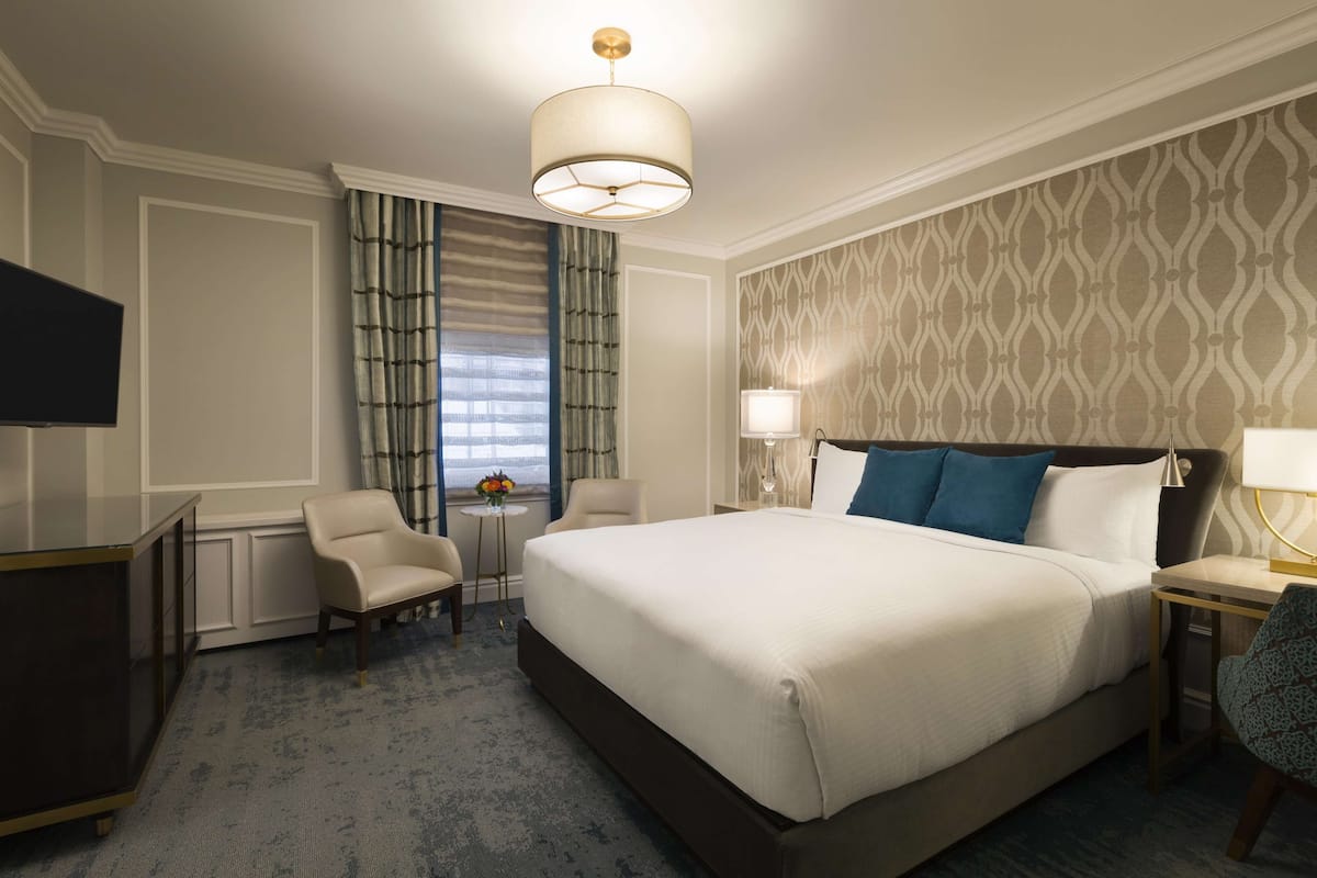 A hotel room with a large bed, a desk, a chair, a television, and a window with curtains.