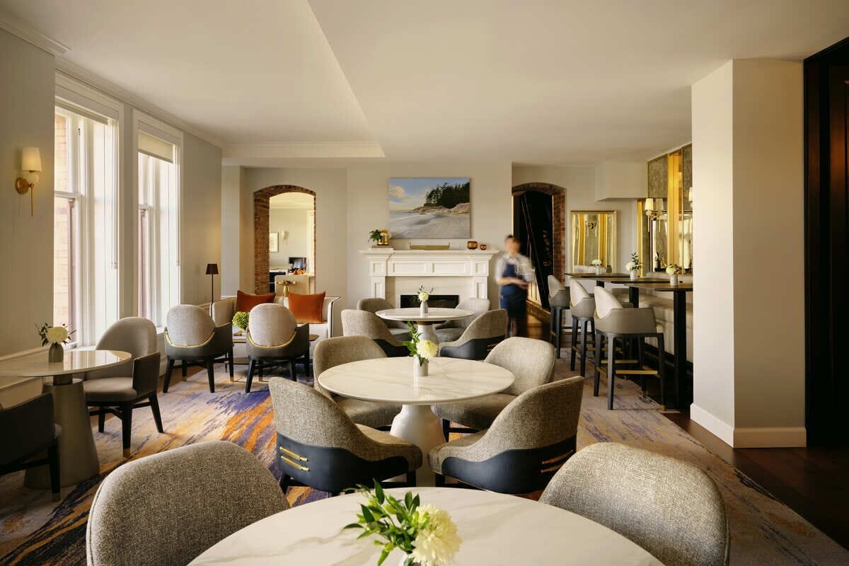 A hotel lobby with round tables, chairs, a fireplace, and a bar area.