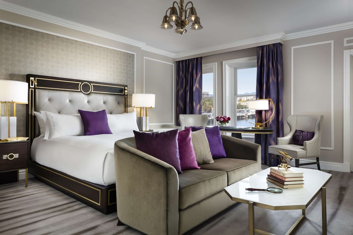 A hotel room with a large bed, a sofa, a coffee table, and a view of the city.