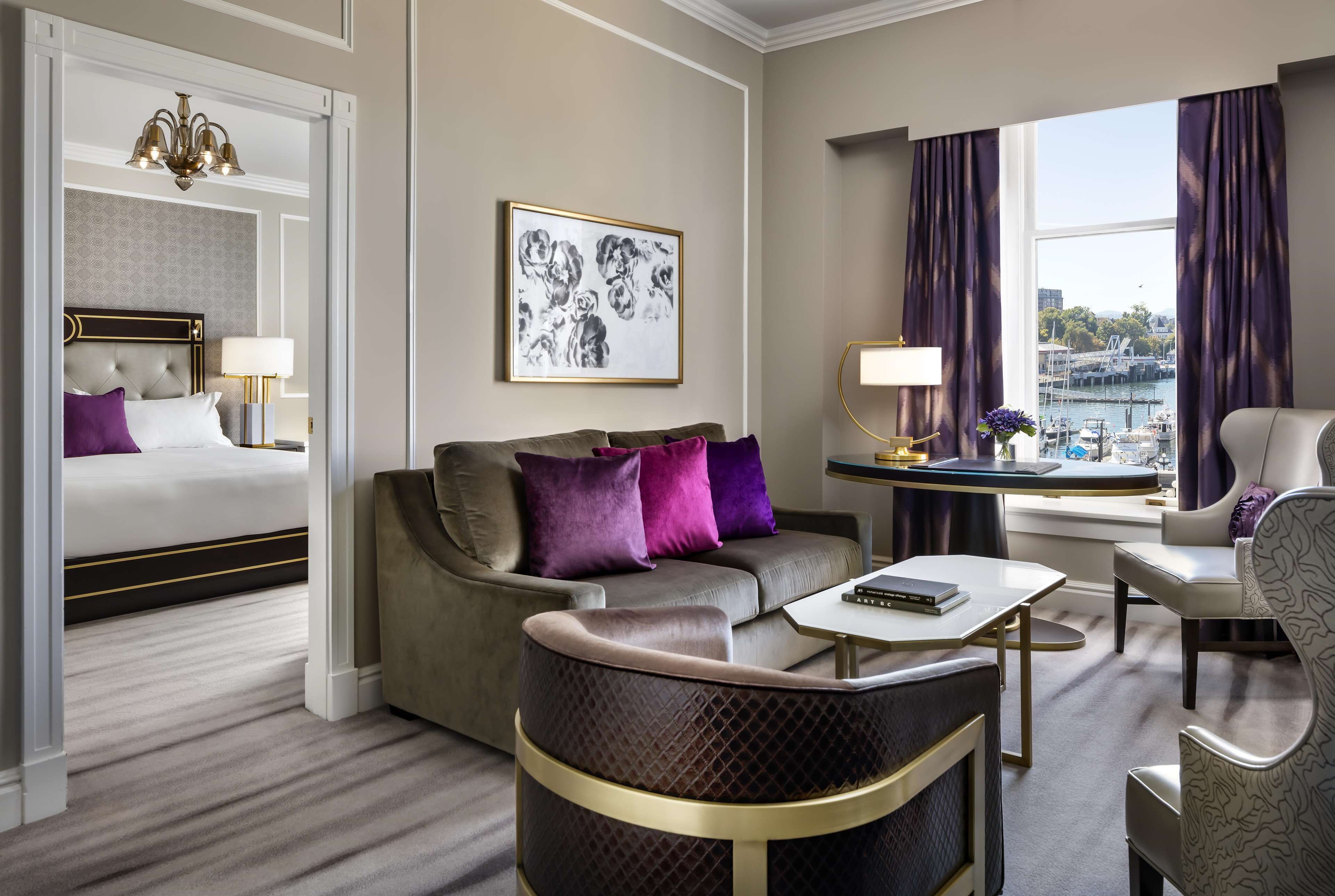 A hotel room with a bed, sofa, armchair, and a view of the harbor.