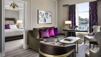 A hotel room with a bed, sofa, armchair, and a view of the harbor.
