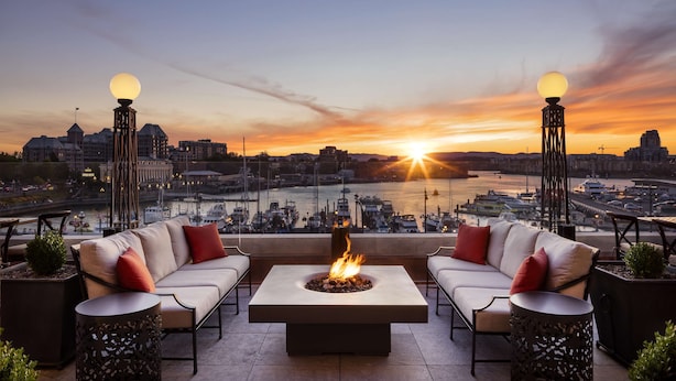 A rooftop terrace with a fire pit, seating, and a view of the cityscape at sunset. - Fairmont Empress (Victoria)