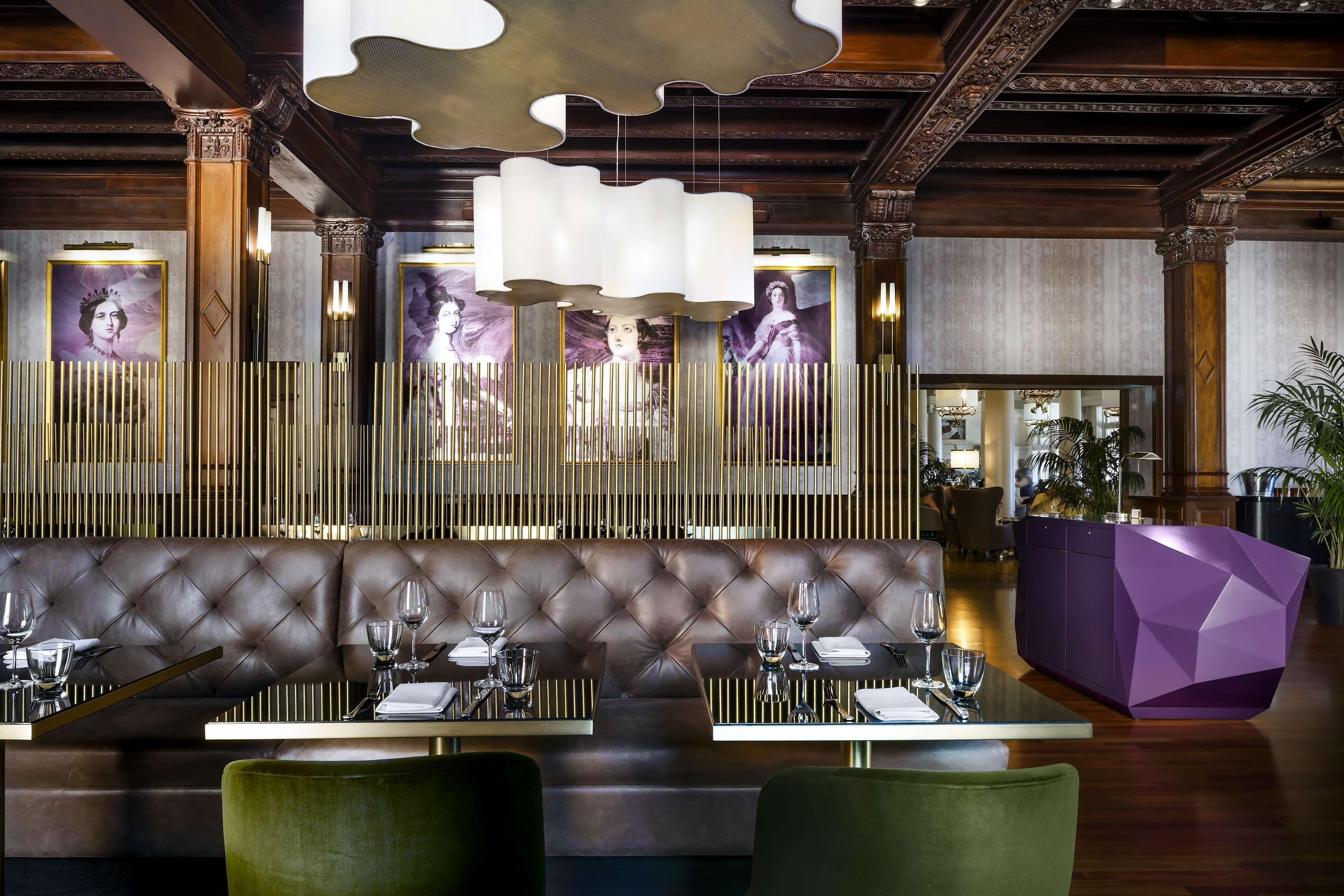 Een restaurant met een gestoffeerde lederen zithoek, moderne hanglampen en een geometrisch paarse accentmuur.
