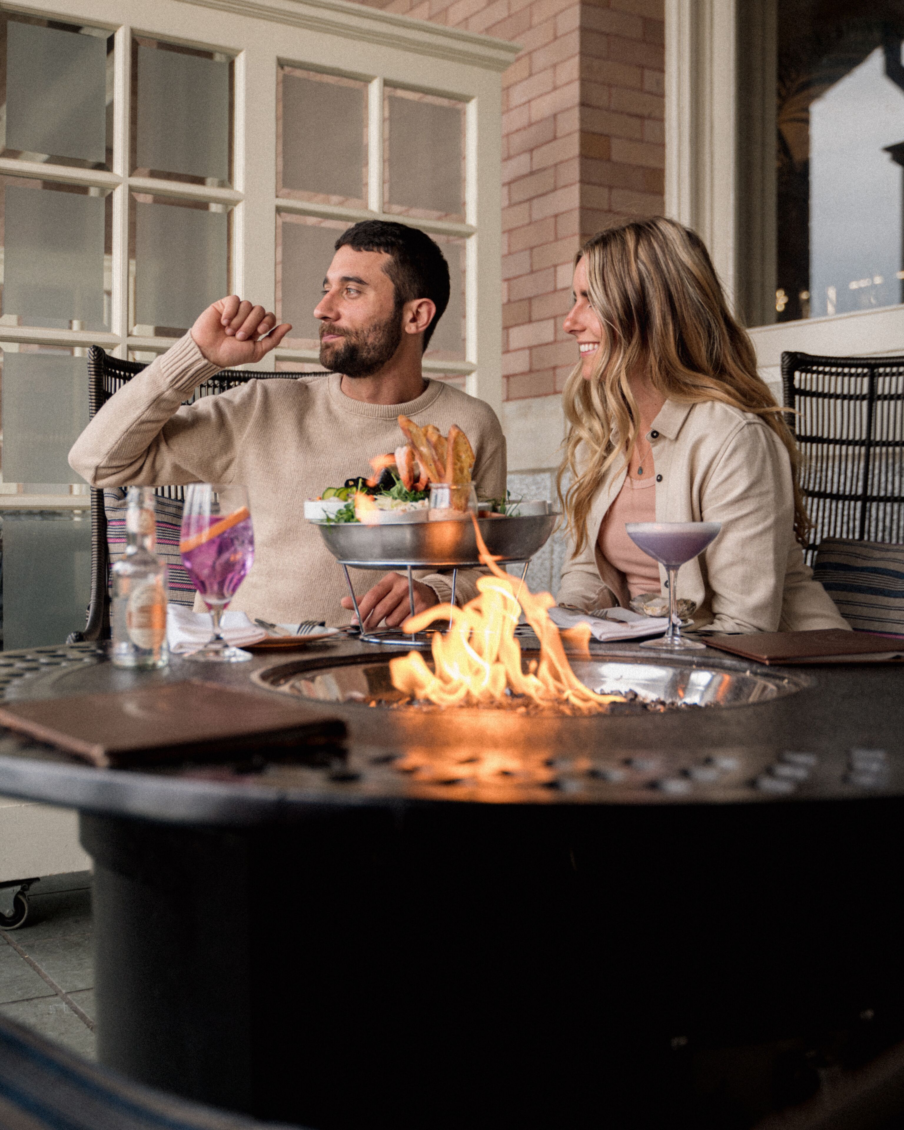 A couple dining at an outdoor table with a fire feature in the center.