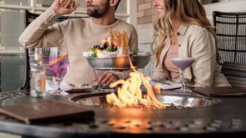 A couple dining at an outdoor table with a fire feature in the center.