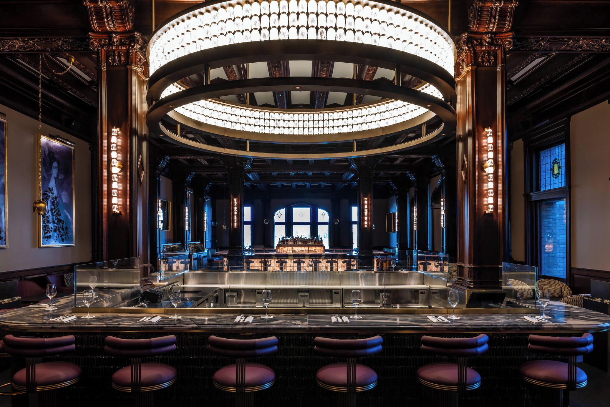 A bar area with a marble counter, bar stools, and a chandelier.