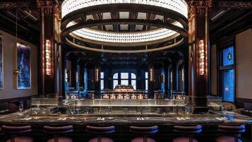 A bar area with a marble counter, bar stools, and a chandelier.
