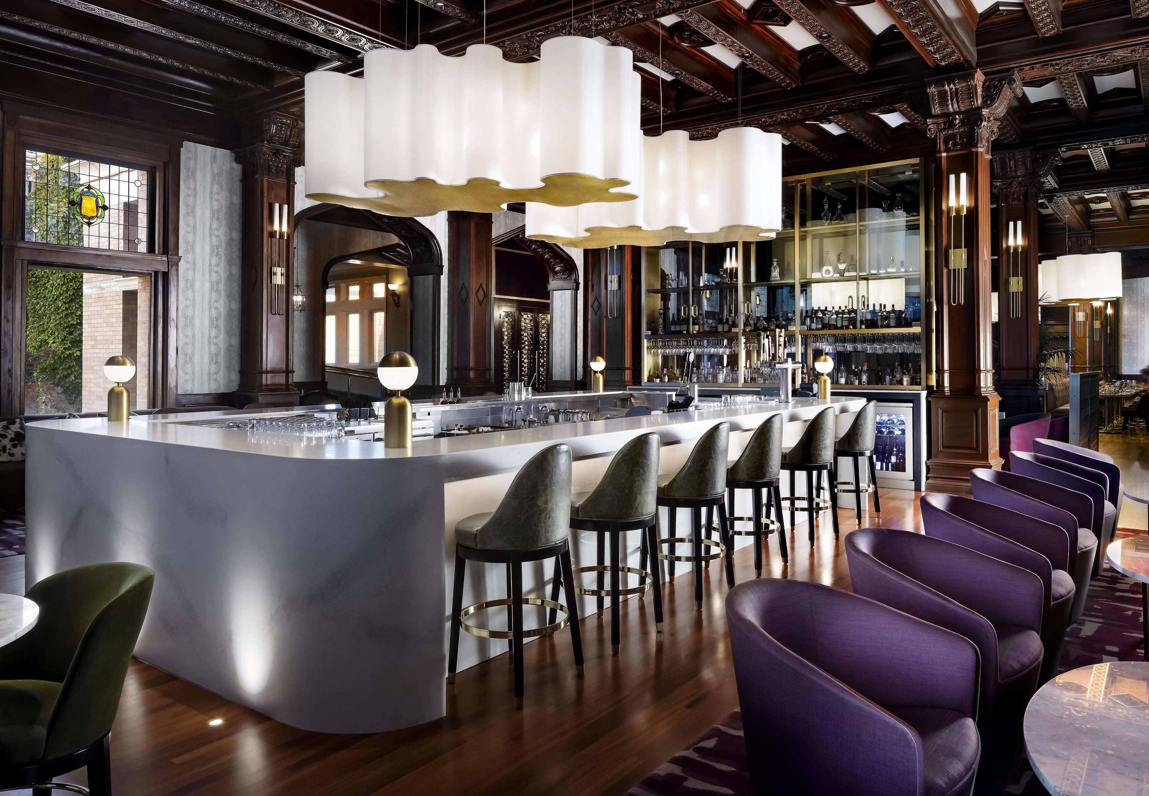 A bar area with a central island, bar stools, and a seating area with round tables.