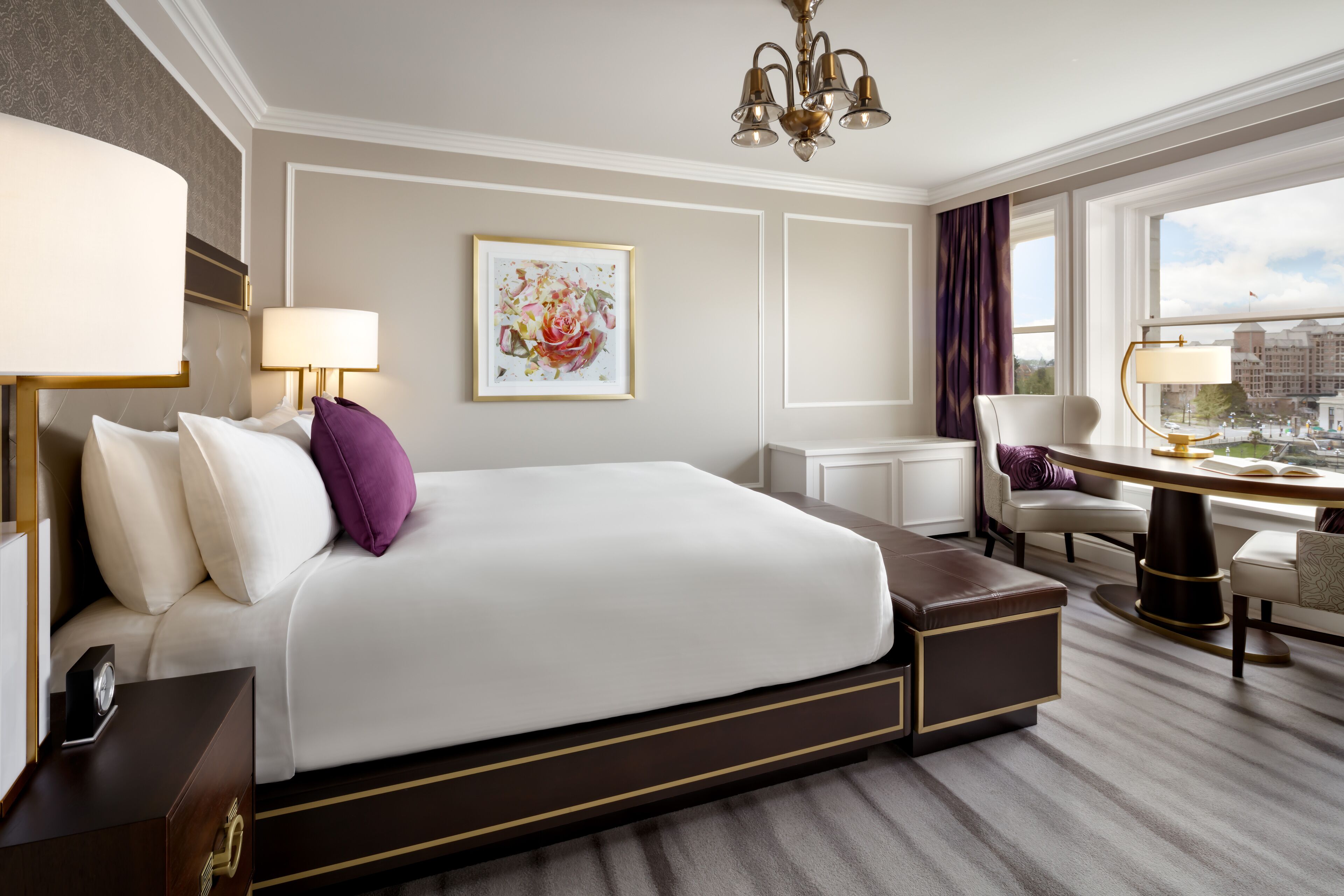 A hotel room with a large bed, a desk with a lamp, a chair, and a view of the city through the window.