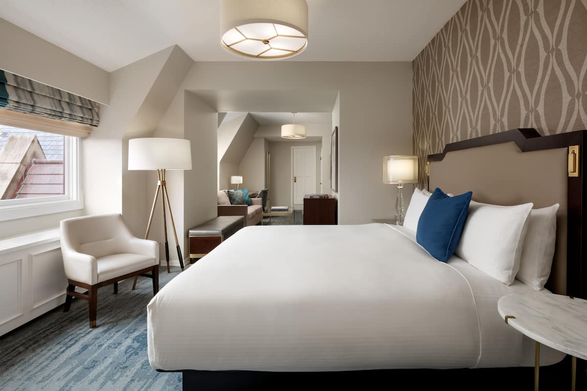 A hotel room with a large bed, a chair, a desk, and a lamp.