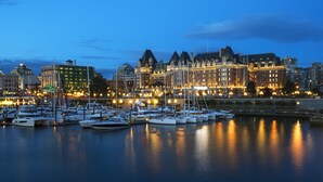 A marina with boats docked, a waterfront hotel with multiple stories, and a cityscape in the background. - Fairmont Empress (Victoria)