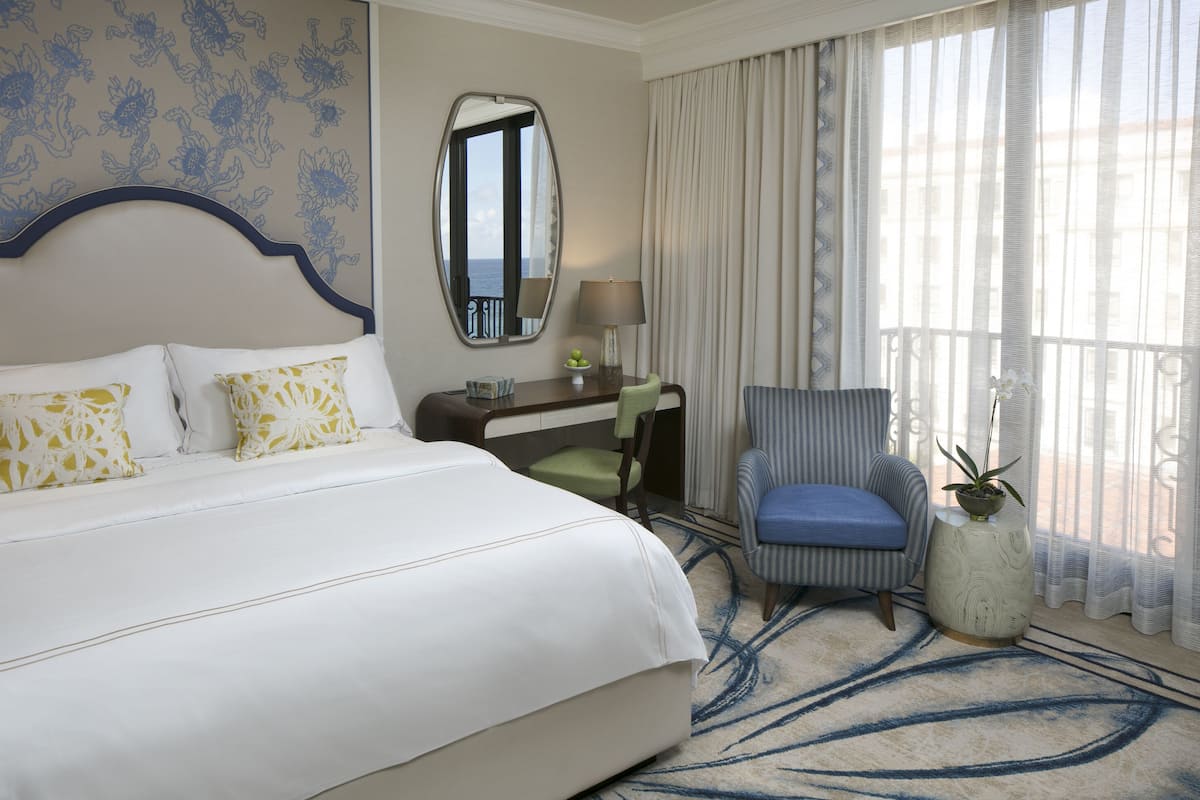Habitación de hotel con una cama grande, un escritorio, una silla, una planta en maceta y vistas al mar por la ventana.