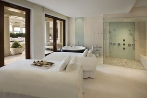 A modern hotel room with a large bed, a separate sitting area, a bathtub, and a glass-enclosed shower area.