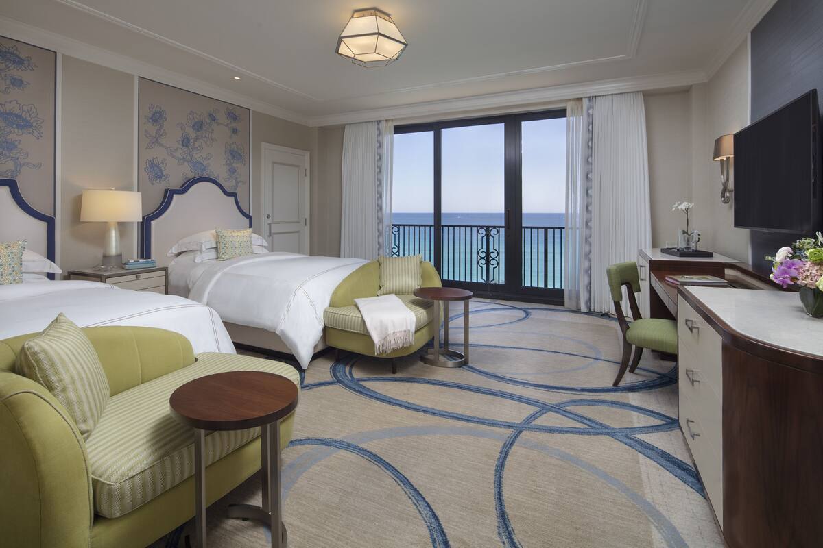 Habitación de hotel con dos camas, un sofá, un escritorio y vista al mar.