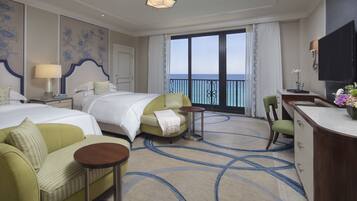 Habitació d'hotel amb dos llits, un sofà, escriptori i vista al mar.