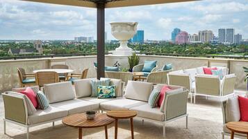 A rooftop terrace with wicker furniture, a large white urn, and a city view.