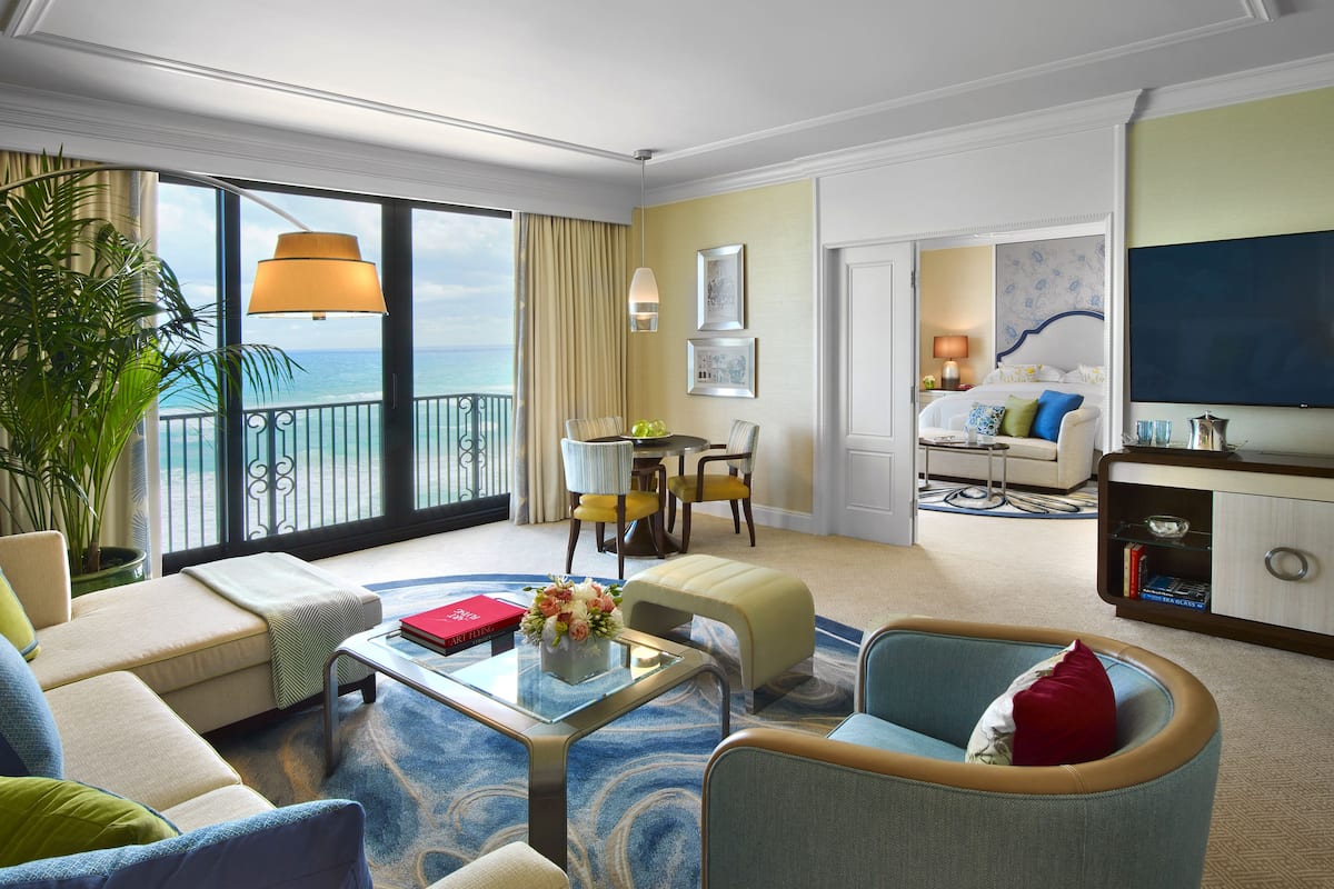 Una habitación de hotel con balcón, comedor, sala de estar y televisión.