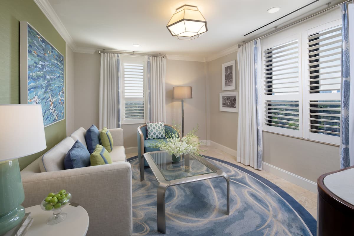 Una sala de estar moderna con una mesa de centro de vidrio, un sofá con cojines estampados, una lámpara de pie y un cuadro abstracto grande en la pared.
