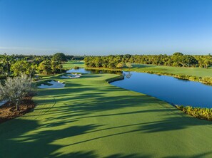 A golf course with a pond, trees, and a clear sky.