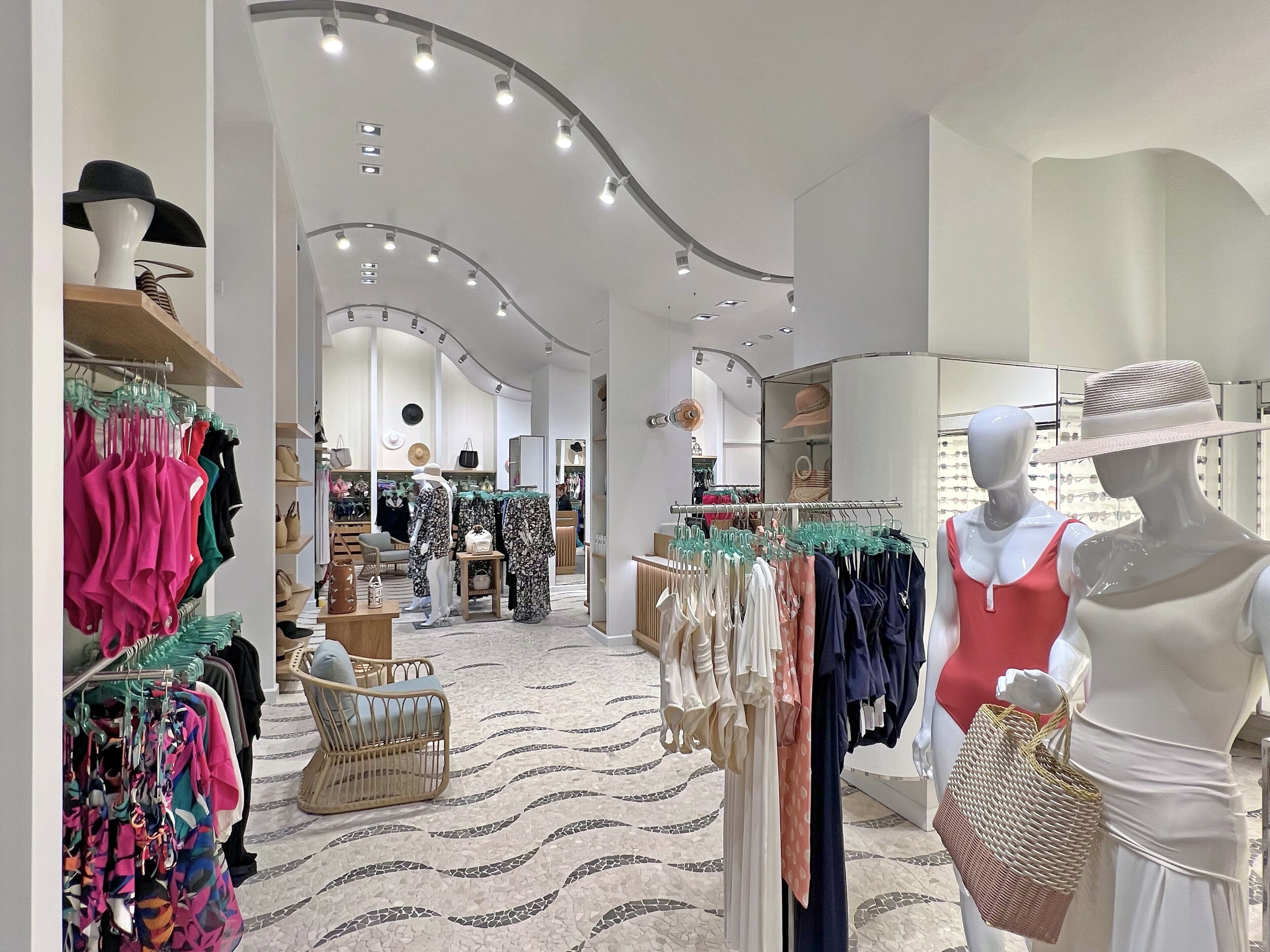 Ein modernes Boutique-Geschäft mit Schaufensterpuppen, die Kleider und Accessoires präsentieren, einem gemusterten Boden und einem gut beleuchteten Innenraum.