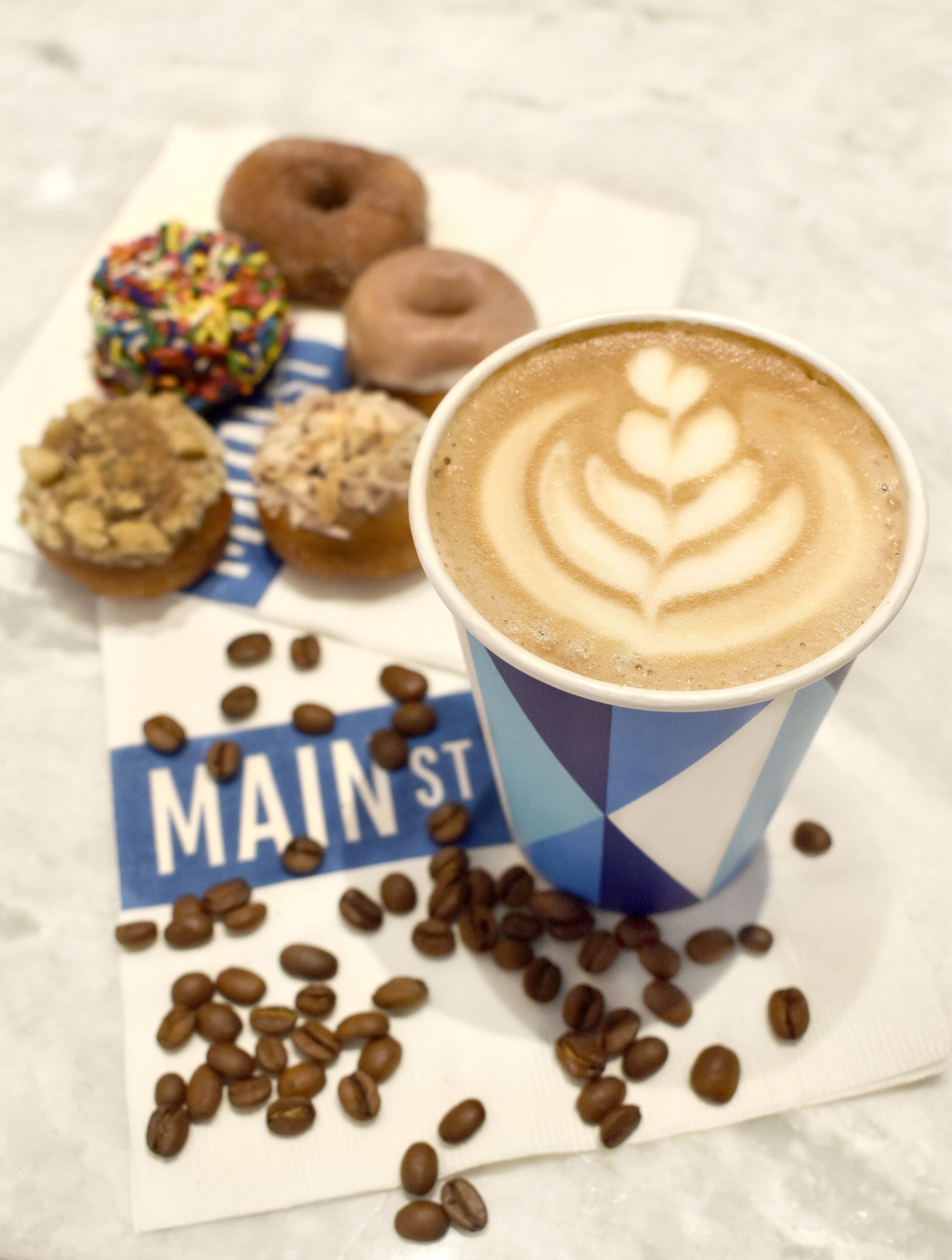 Una taza de café con arte de leche, un letrero que dice "MAINST" y varias pastas y granos de café sobre una mesa.