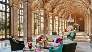 A grand hallway with high ceilings, large windows, and ornate columns. Furnished with elegant chairs and a sofa, the space features a floral carpet and a chandelier. - The Breakers Palm Beach (Palm Beach)