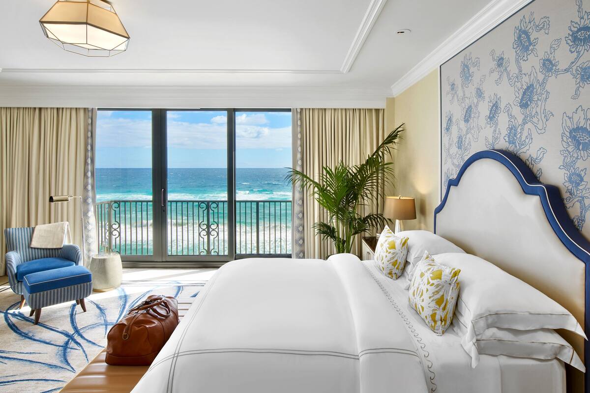 Habitación de hotel con una cama grande, una silla, una mesa, una lámpara y vistas al océano.