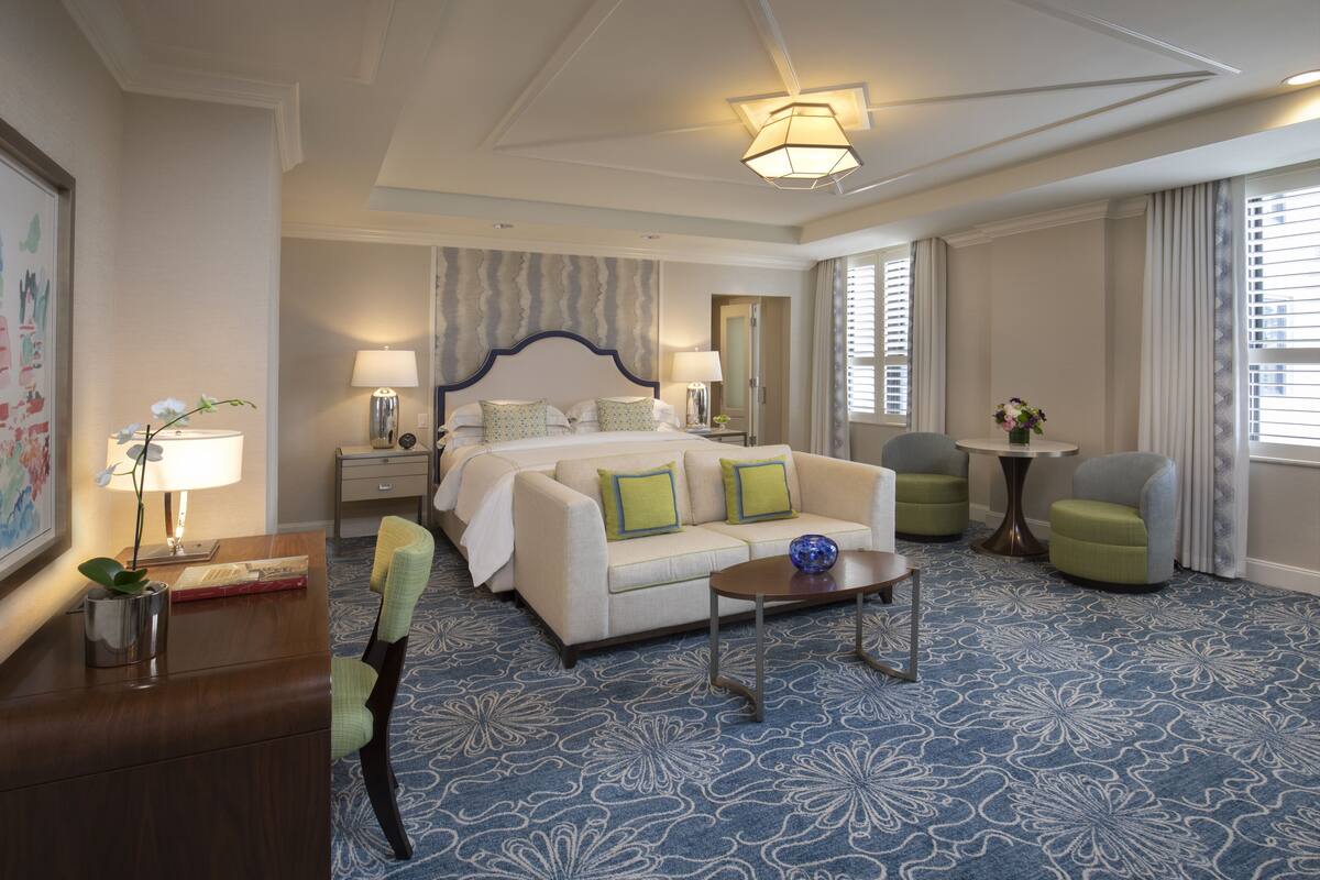 Habitación de hotel con una cama grande, un sofá, una mesita de centro y un escritorio con lámpara.