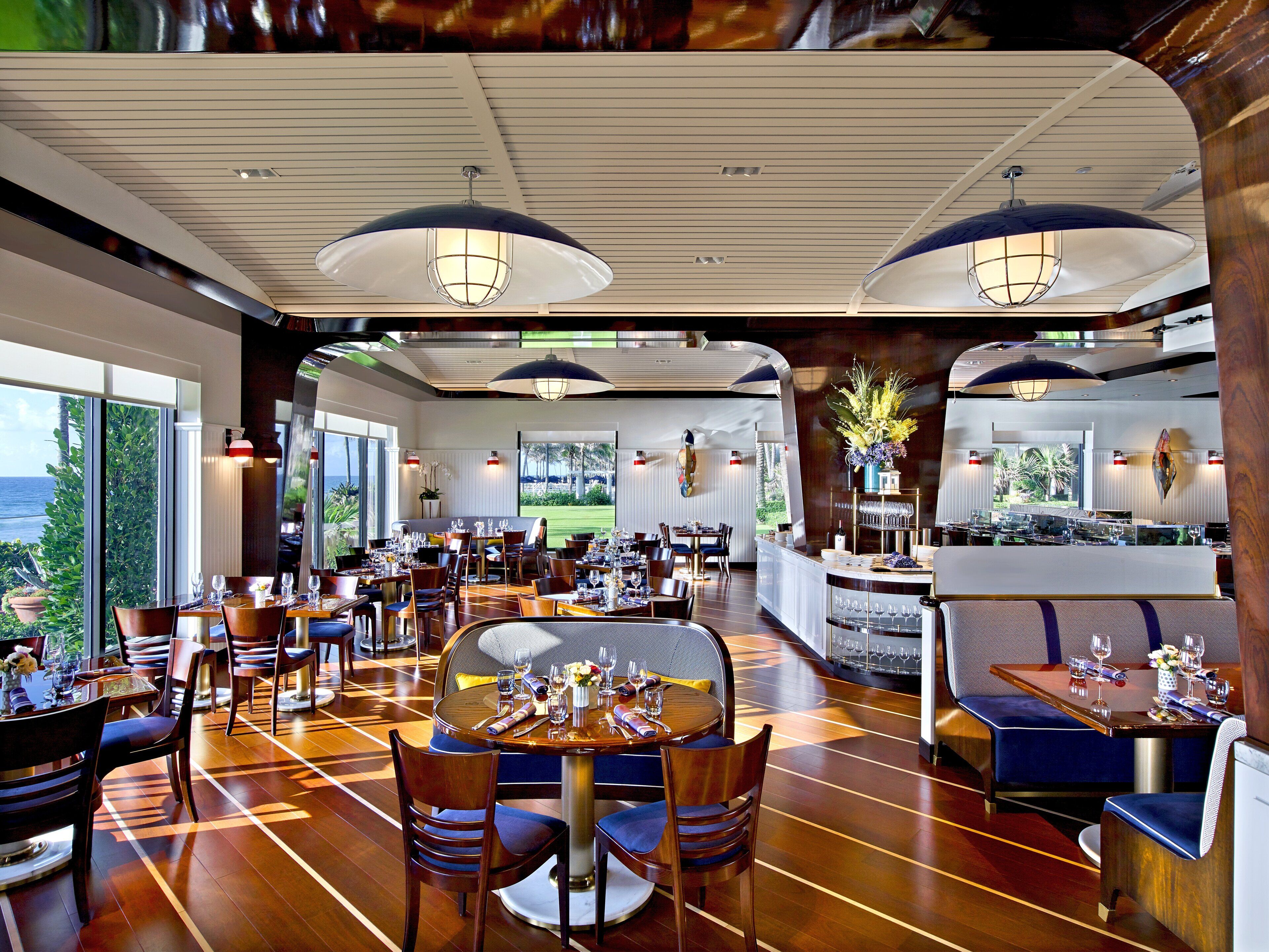 Un restaurante amplio con varias zonas de comedor, ventanas grandes que ofrecen vistas al exterior e iluminación moderna.