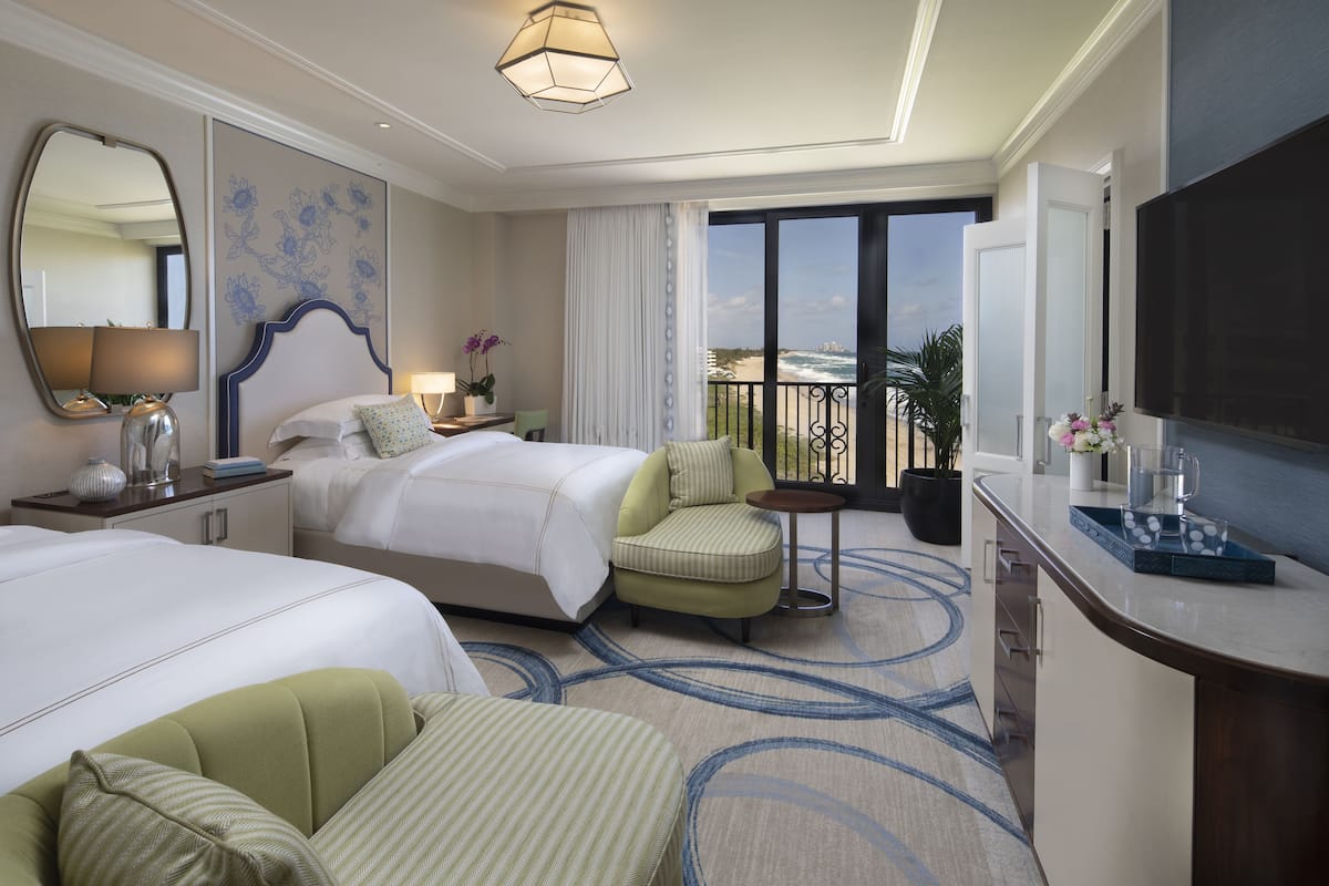 Habitación de hotel con dos camas, zona de estar, balcón con vistas y televisión de pantalla plana.
