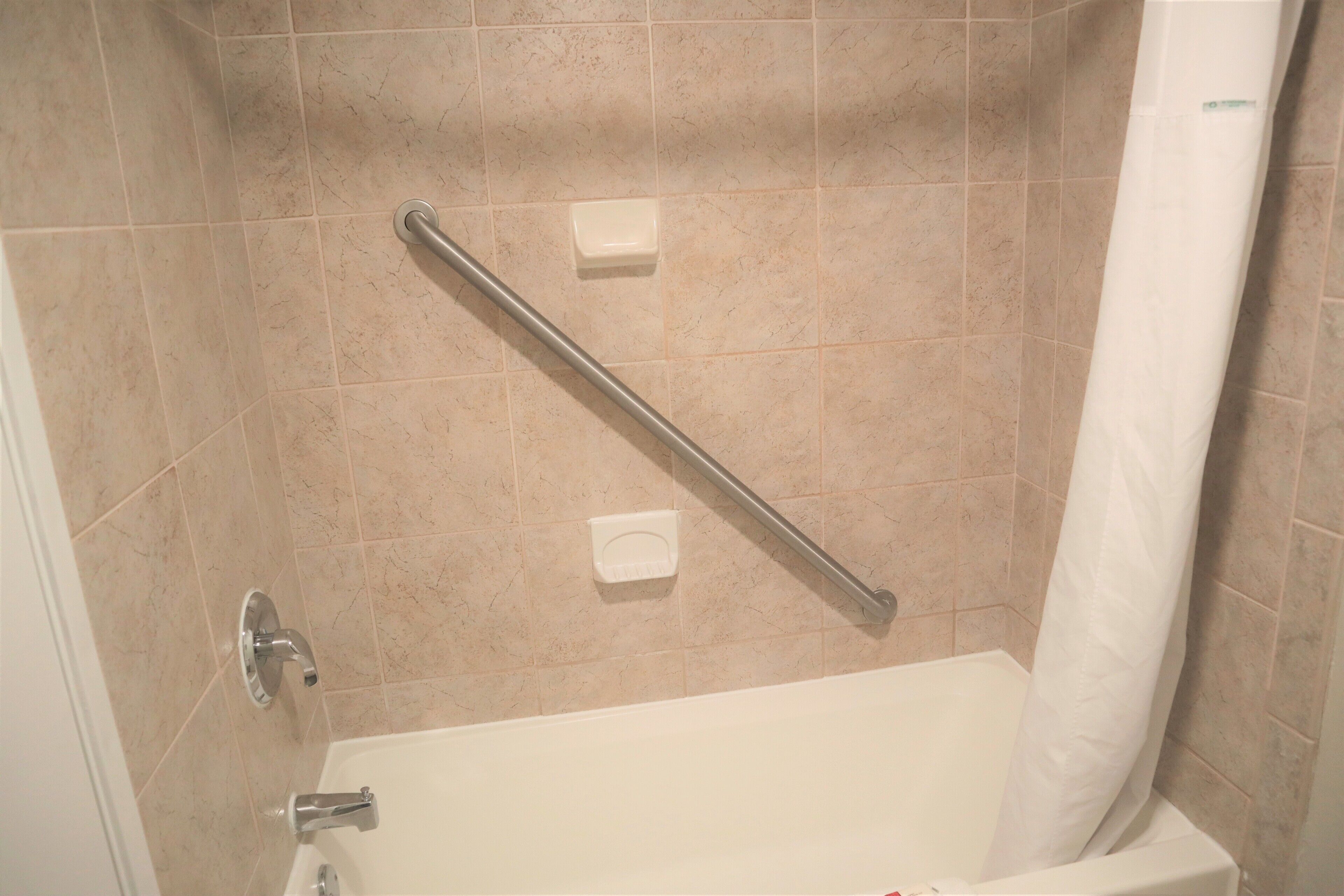 Un baño con bañera, barras de apoyo y cortina de ducha.