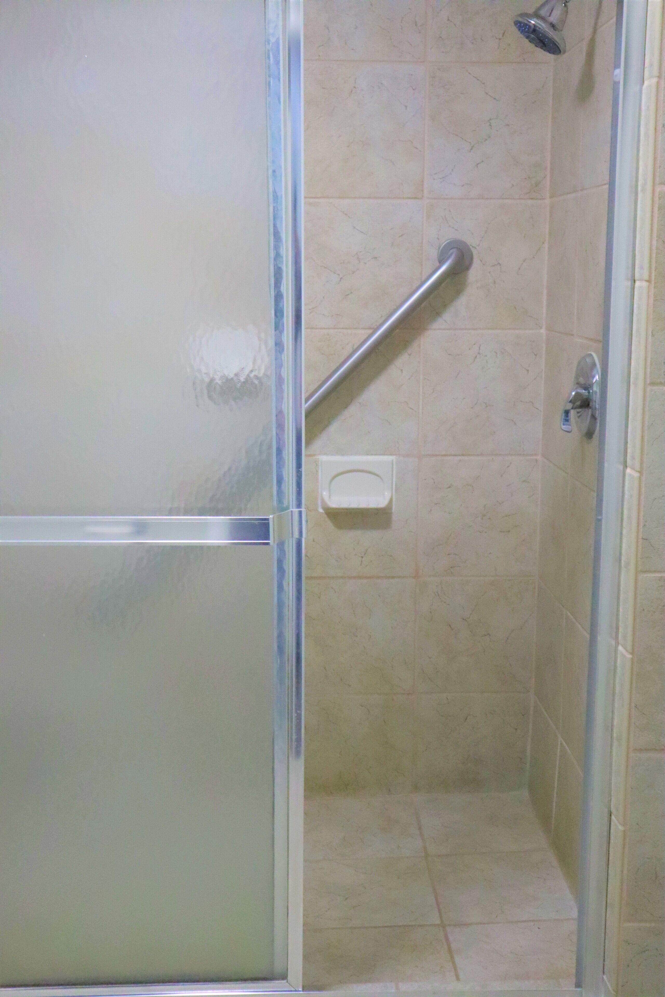 A shower with a glass door, a handrail, and a tiled wall.