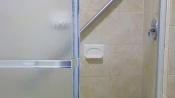 A shower with a glass door, a handrail, and a tiled wall.