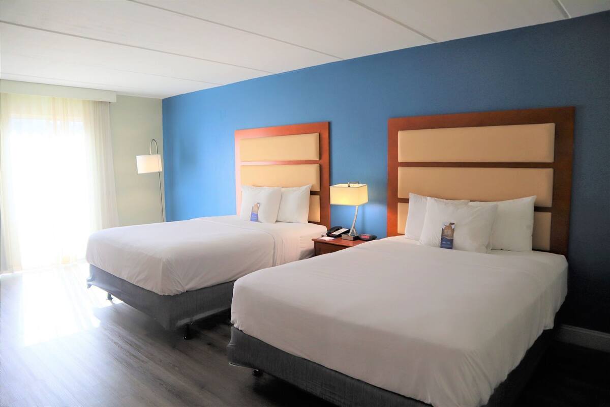 Une chambre d’hôtel avec deux lits, une table de chevet avec une lampe et une fenêtre avec des rideaux.