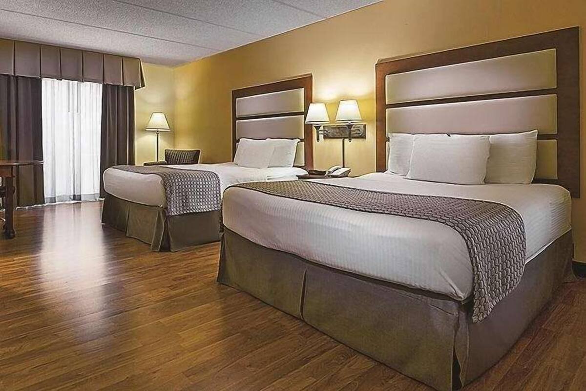 Une chambre d’hôtel avec deux lits, un plancher en bois et une fenêtre avec des rideaux.