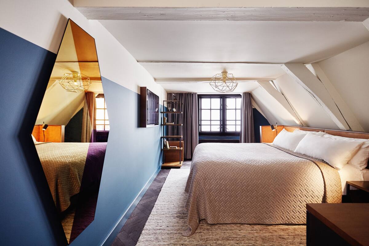 Un dormitorio con una cama grande, un espejo y un techo con vigas a la vista.