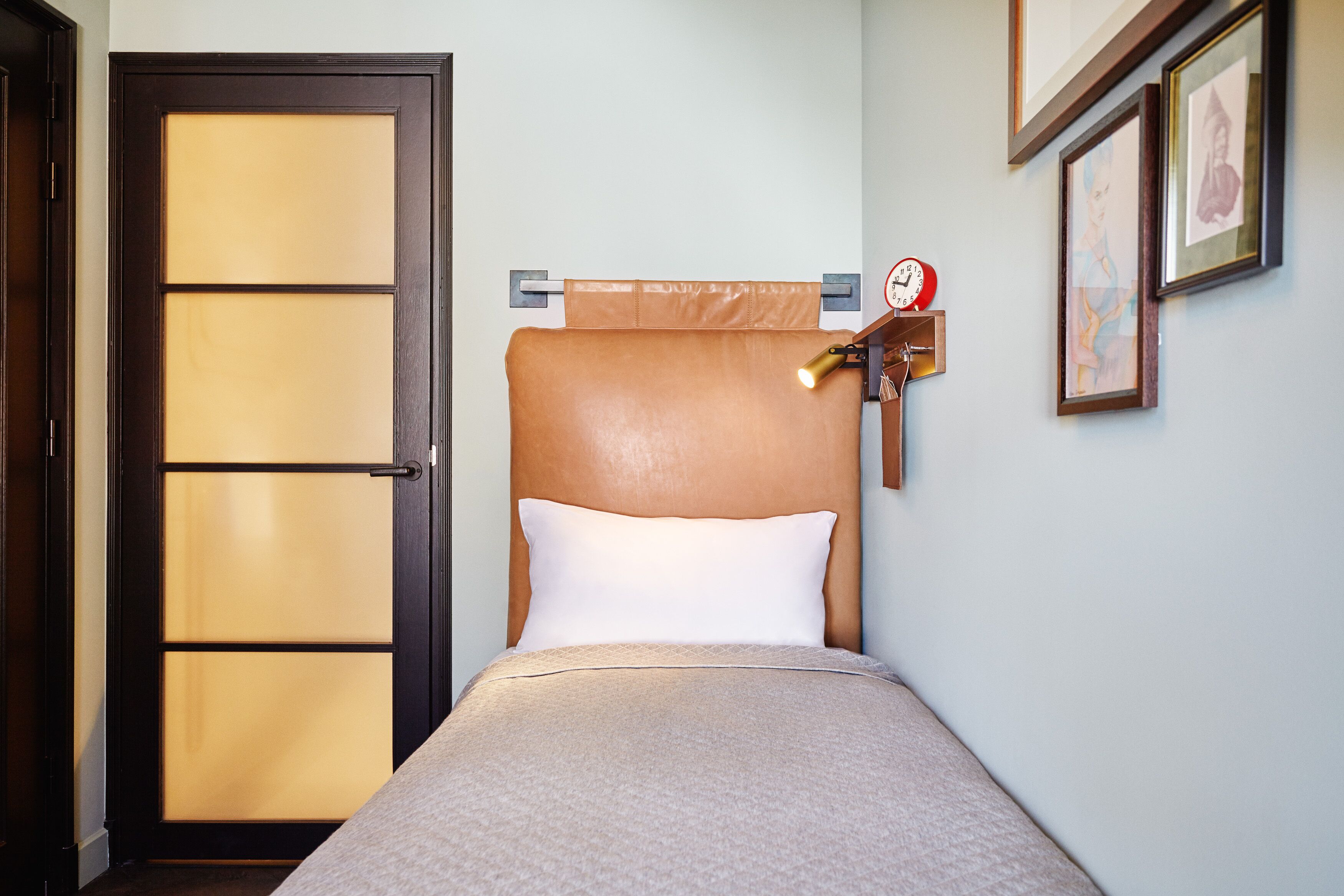 Una habitación de hotel con una cama, cabecera de madera, un reloj y cuadros en la pared.