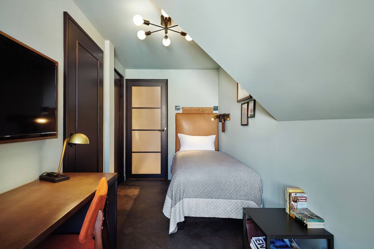 Un dormitorio con cama, escritorio, silla y televisor montado en la pared.