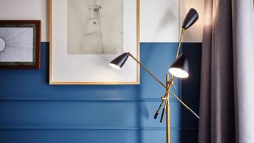 A room with a blue wall, a framed drawing, and a floor lamp.
