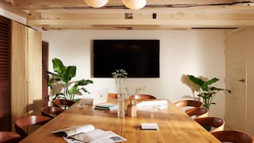 Un salón de conferencias con una mesa de madera, sillas, una computadora portátil, un jarrón con flores y un televisor de pantalla plana grande en la pared.