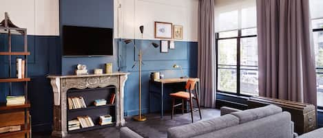 A room with a fireplace, a desk, a bookshelf, a sofa, and a large window with curtains.