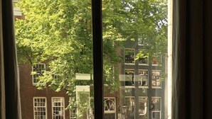 Vista desde una ventana de un edificio con fachada de ladrillo, un árbol y coches aparcados.