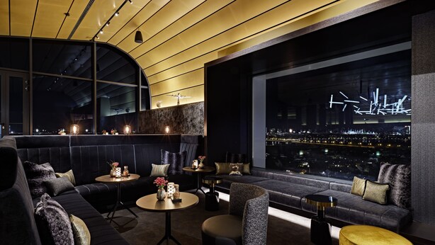 Un salón moderno con un sofá de color oscuro, una mesa redonda y vistas a un paisaje urbano nocturno.