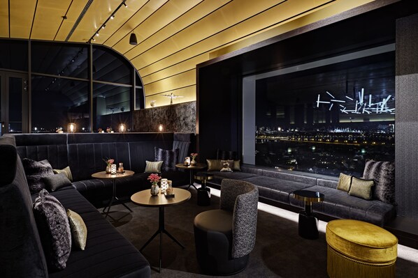 A modern lounge with a dark-colored sofa, a round table, and a view of a cityscape at night. - Lindner Dusseldorf Seestern, Part of JdV by Hyatt (Düsseldorf)
