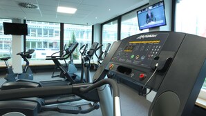 Un gimnasio con cintas de correr, bicicletas estáticas y una pantalla de televisión mostrando un noticiero.