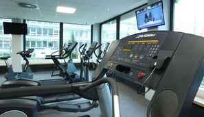 A gym with treadmills, stationary bikes, and a TV screen displaying a news channel. - Lindner Dusseldorf Seestern, Part of JdV by Hyatt (Düsseldorf)