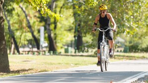 Una persona pedaleando en bicicleta por un sendero pavimentado en un parque.