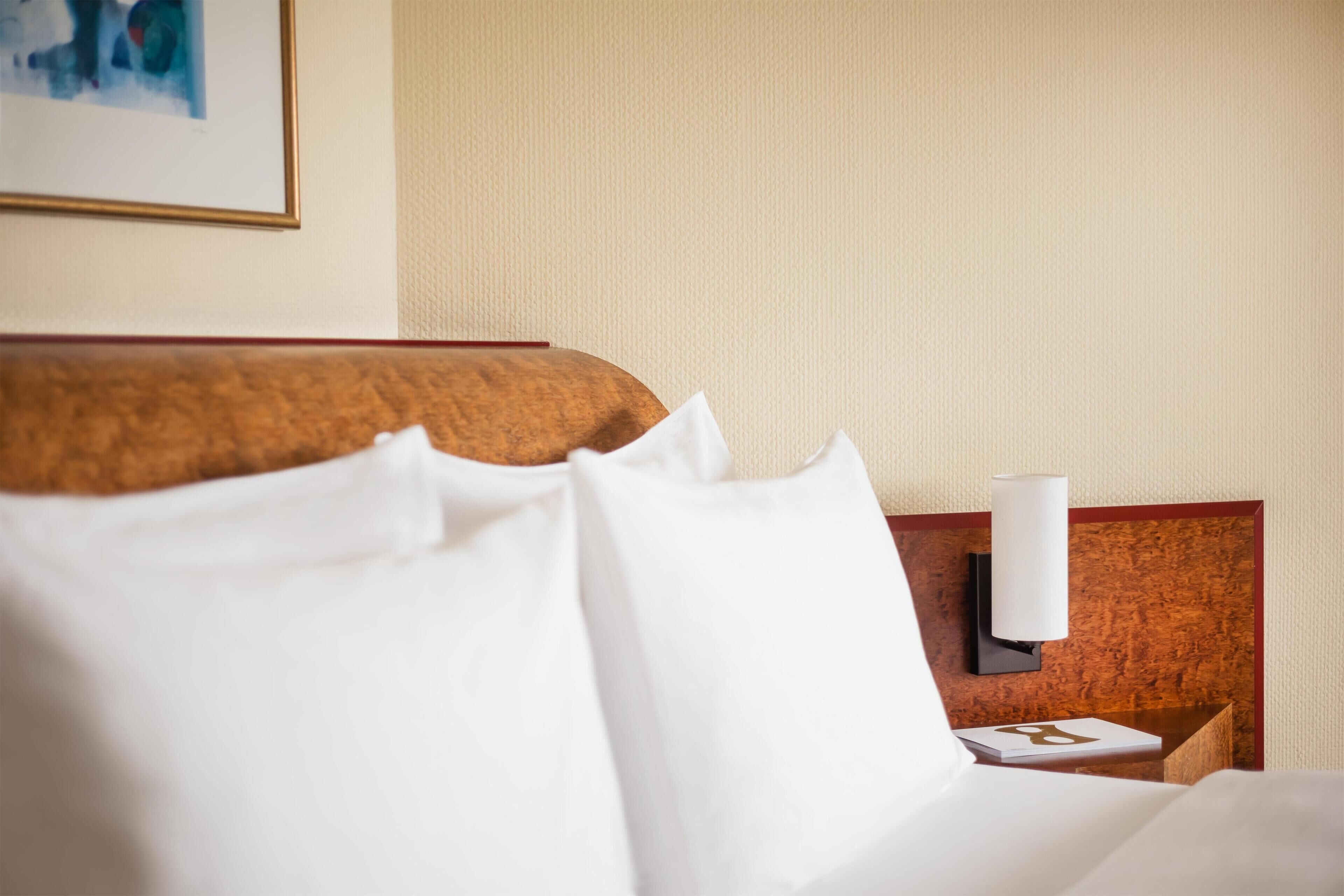 Habitación de hotel con una cama bien hecha, cabecera de madera y mesita de noche de pared con lámpara.